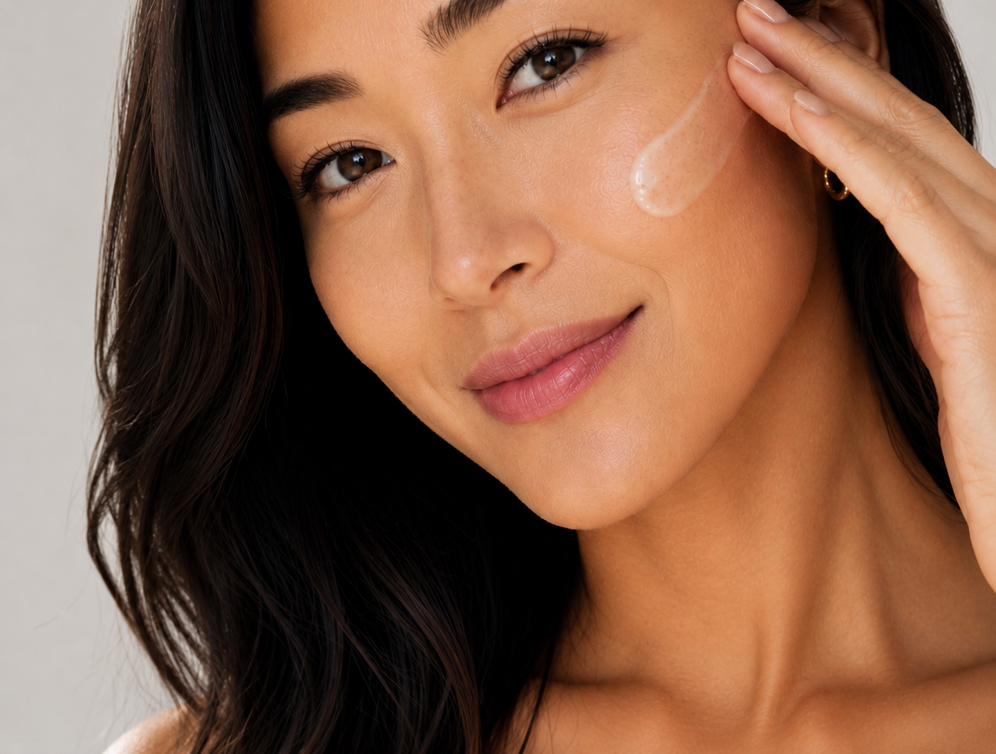 Woman applying skincare product to her face with a neutral background