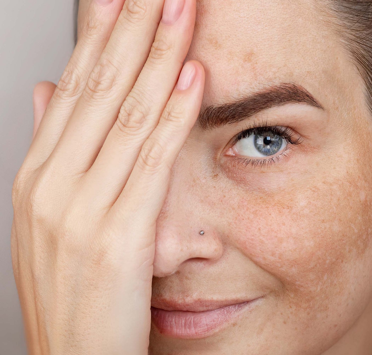 Close-up of a person with a hand covering one eye against a neutral background